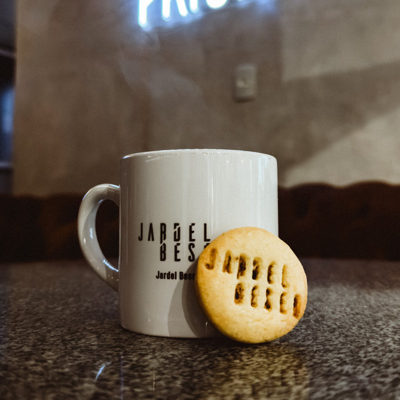 Caneca e biscoito com o logo da barbearia, embaixo do neon