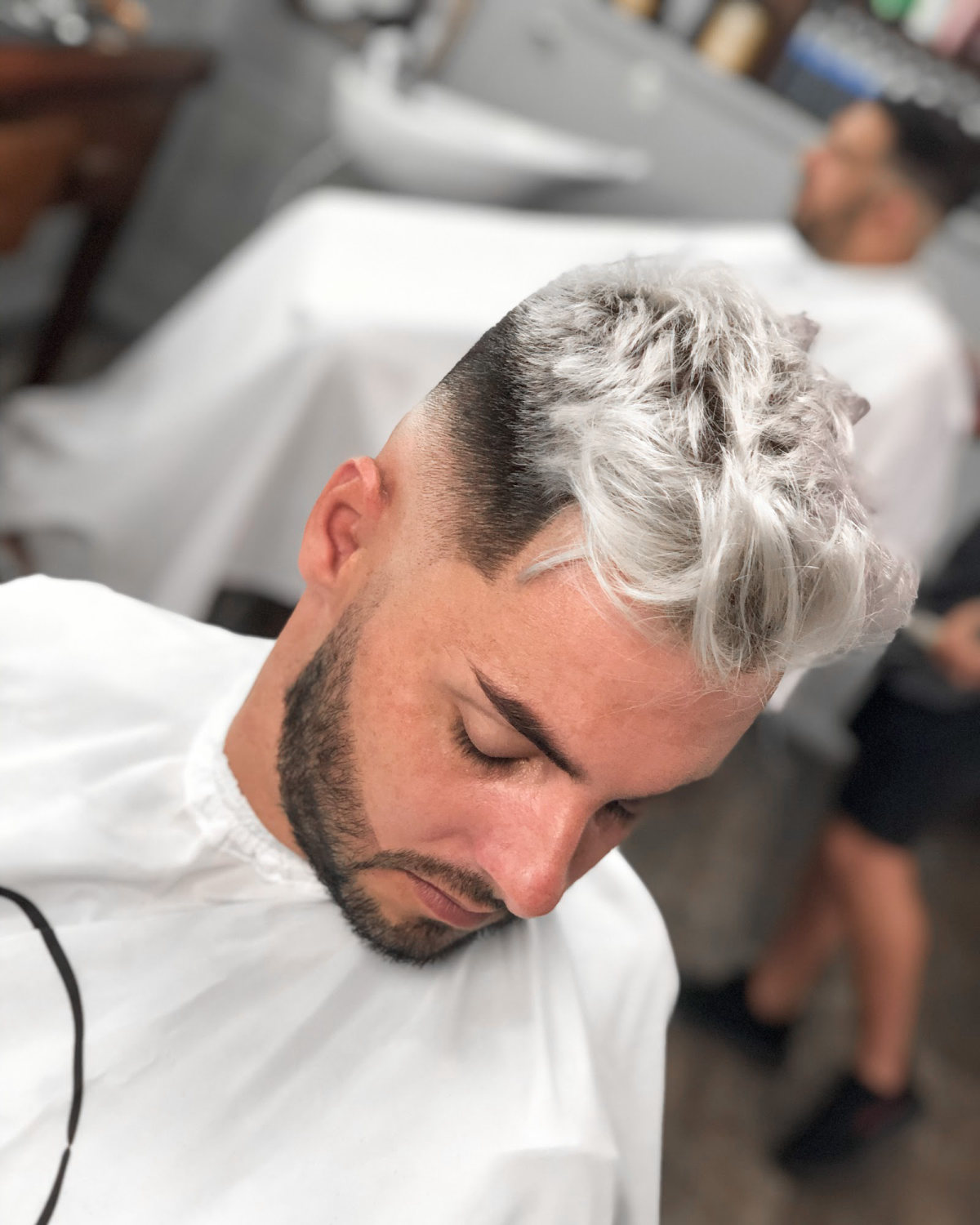 Cliente com o cabelo platinado e degradê, de capa branca na cadeira