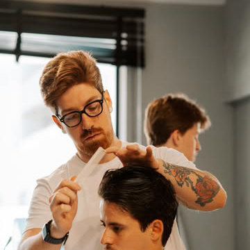 Barbeiro de óculos cortando o cabelo de um cliente