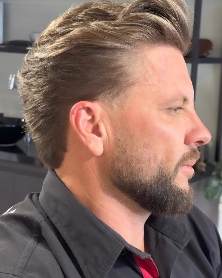 Cliente de perfil com o cabelo penteado pra trás e a barba aparada